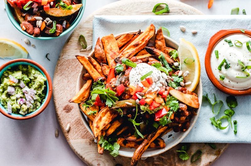 A vibrant platter of savory sweet potato fries with fresh toppings, perfect for a tasty snack.
