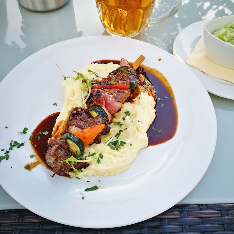 Close-up of delicious kebabs on creamy mashed potatoes drizzled with sauce.