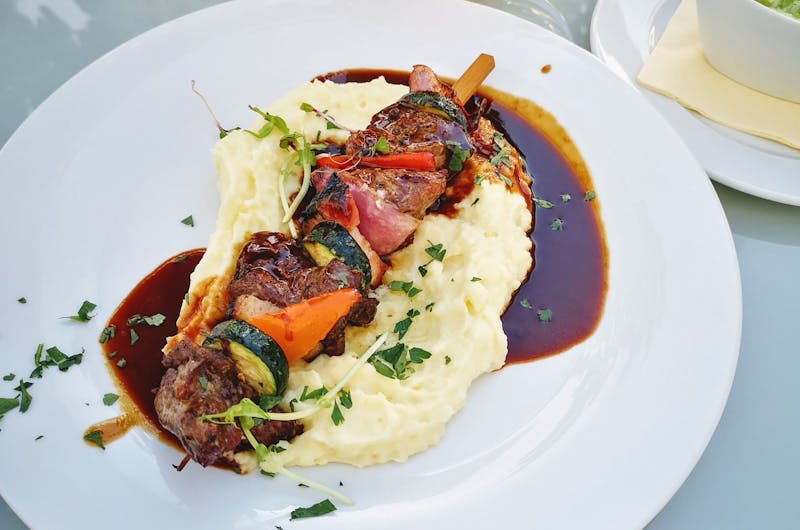 Close-up of delicious kebabs on creamy mashed potatoes drizzled with sauce.