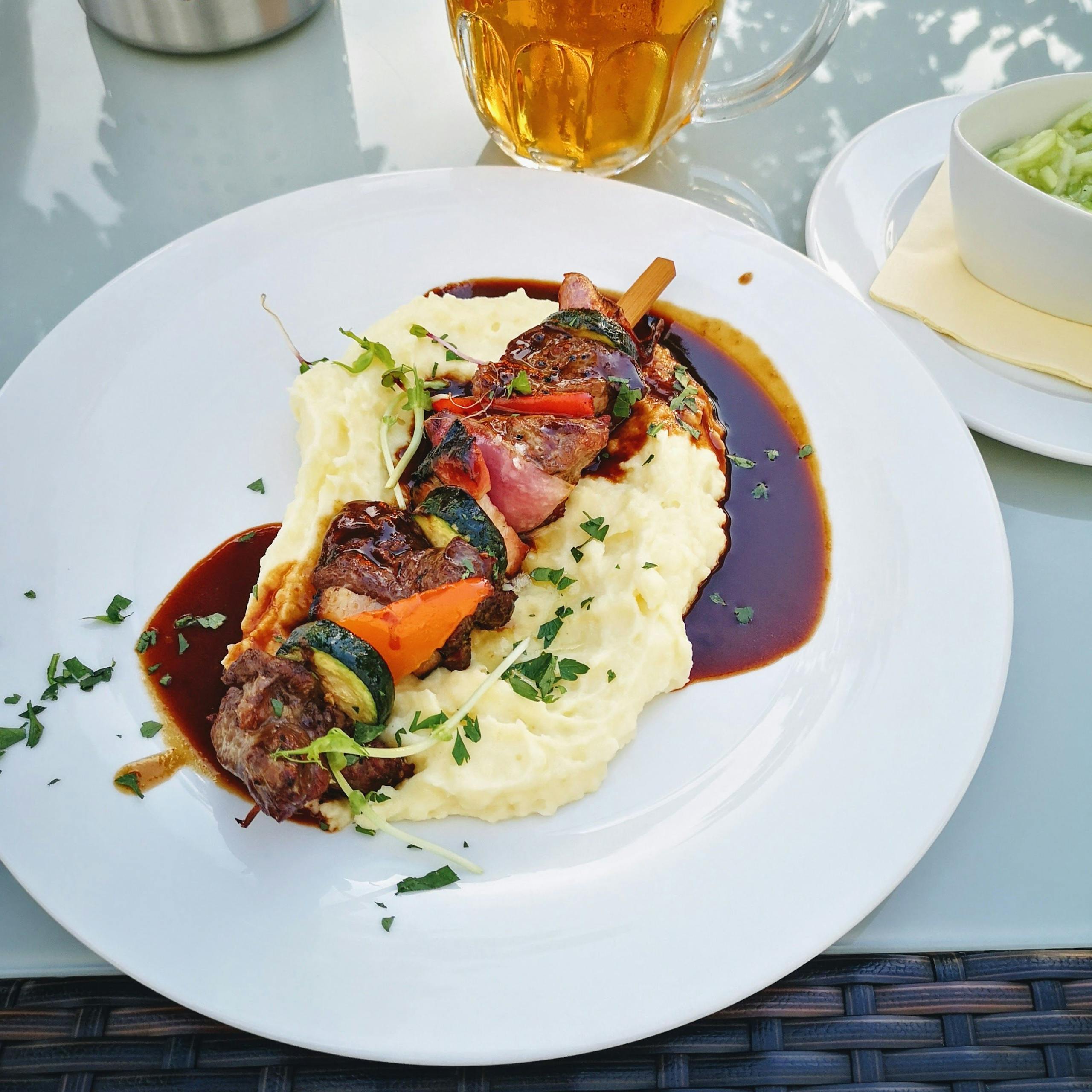 Close-up of delicious kebabs on creamy mashed potatoes drizzled with sauce.