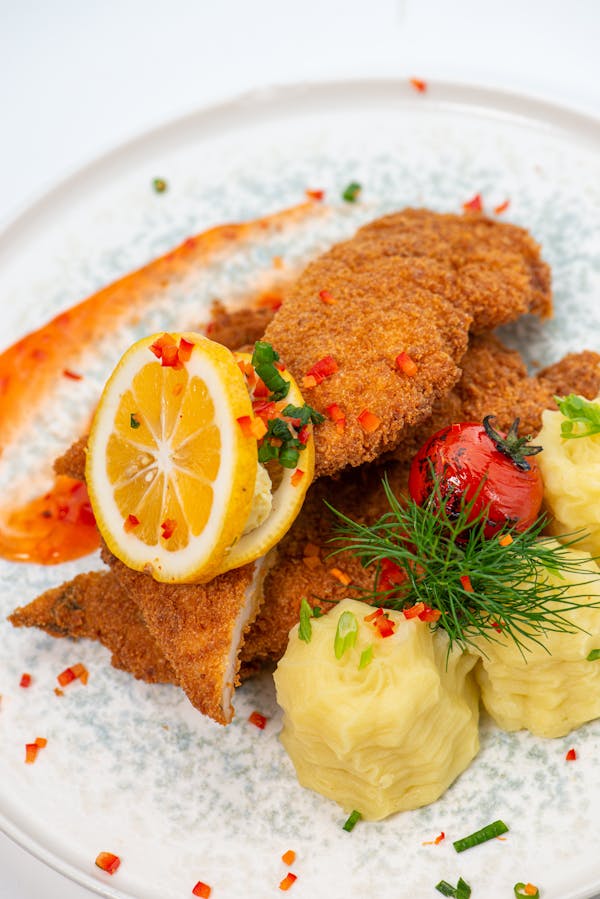 Delicious crispy breaded fish with lemon slice, served with flavorful mashed potatoes and vegetables.