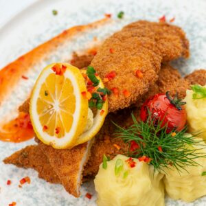 Delicious crispy breaded fish with lemon slice, served with flavorful mashed potatoes and vegetables.